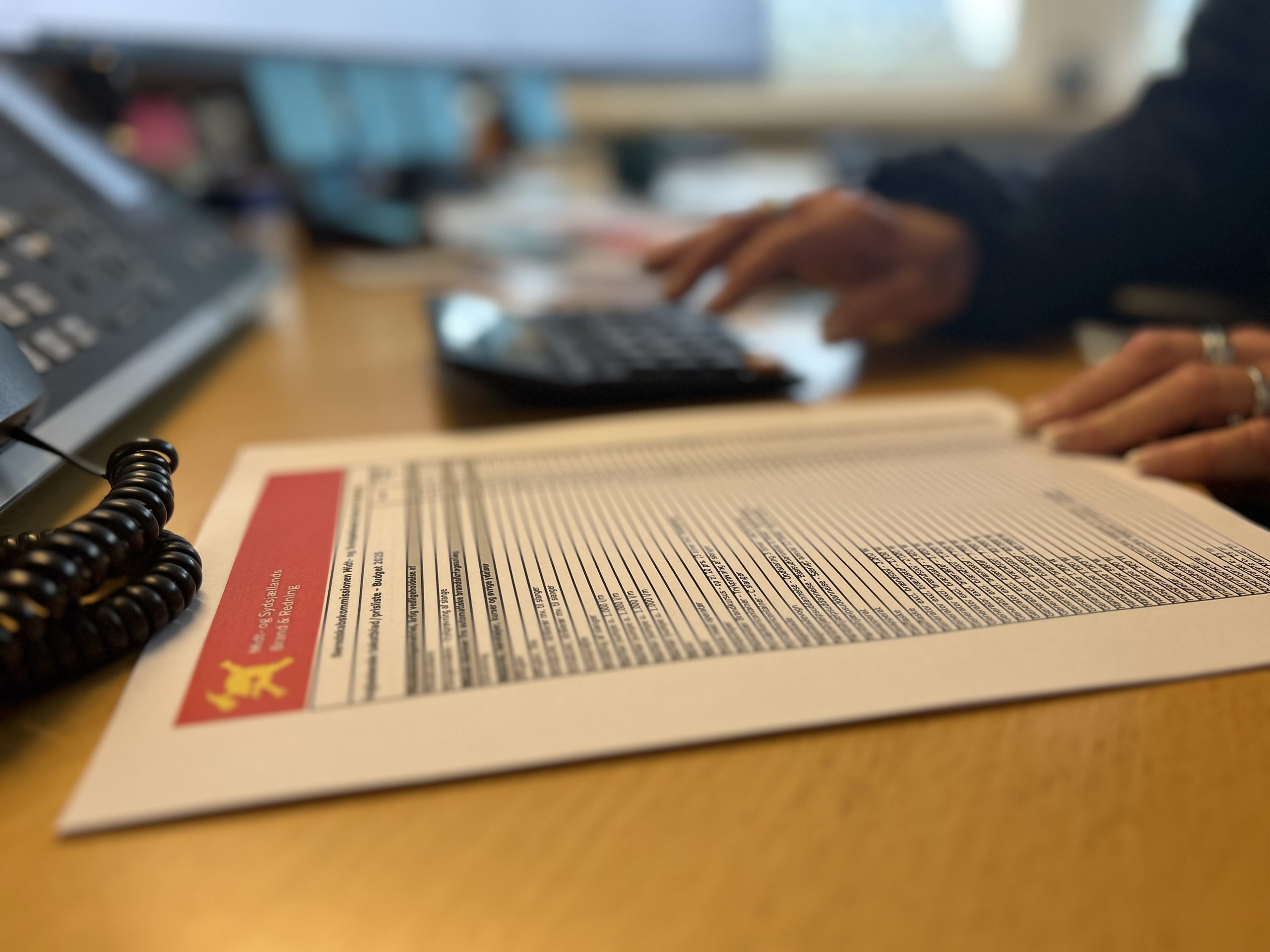 Person arbejder ved skrivebord med papir og lommeregner, fokus på dokument fra Midt- og Sydsjællands Brand & Redning.